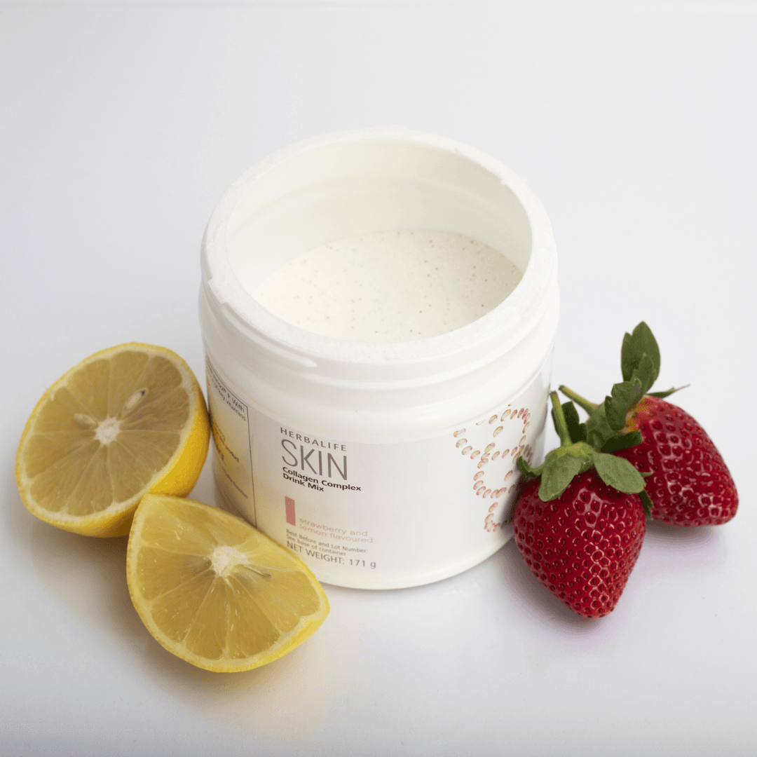 En åpnet boks Herbalife SKIN Collagen Booster står på et bord sammen med to jordbær og en oppskjært sitron.