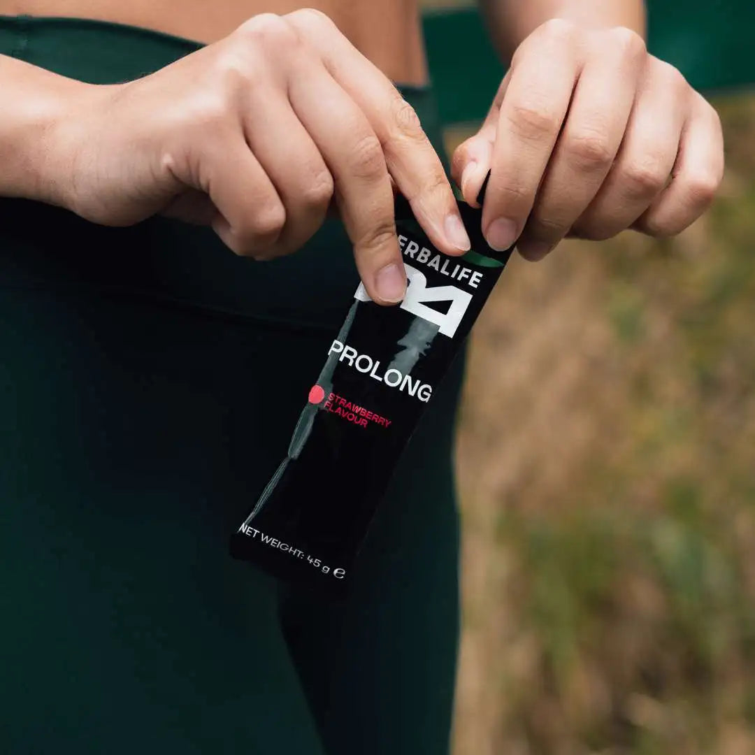 En kvinne i treningsøy som åpner en porsjonspose Herbalife H24 Prolong Energy Gel.