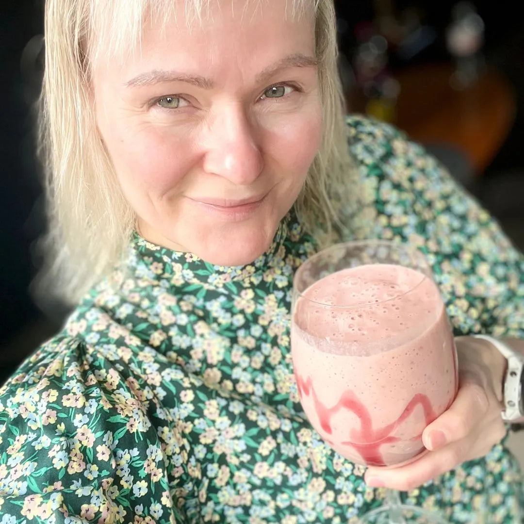 En kvinne holder en rosa Herbalife-shake servert i et stettglass.
