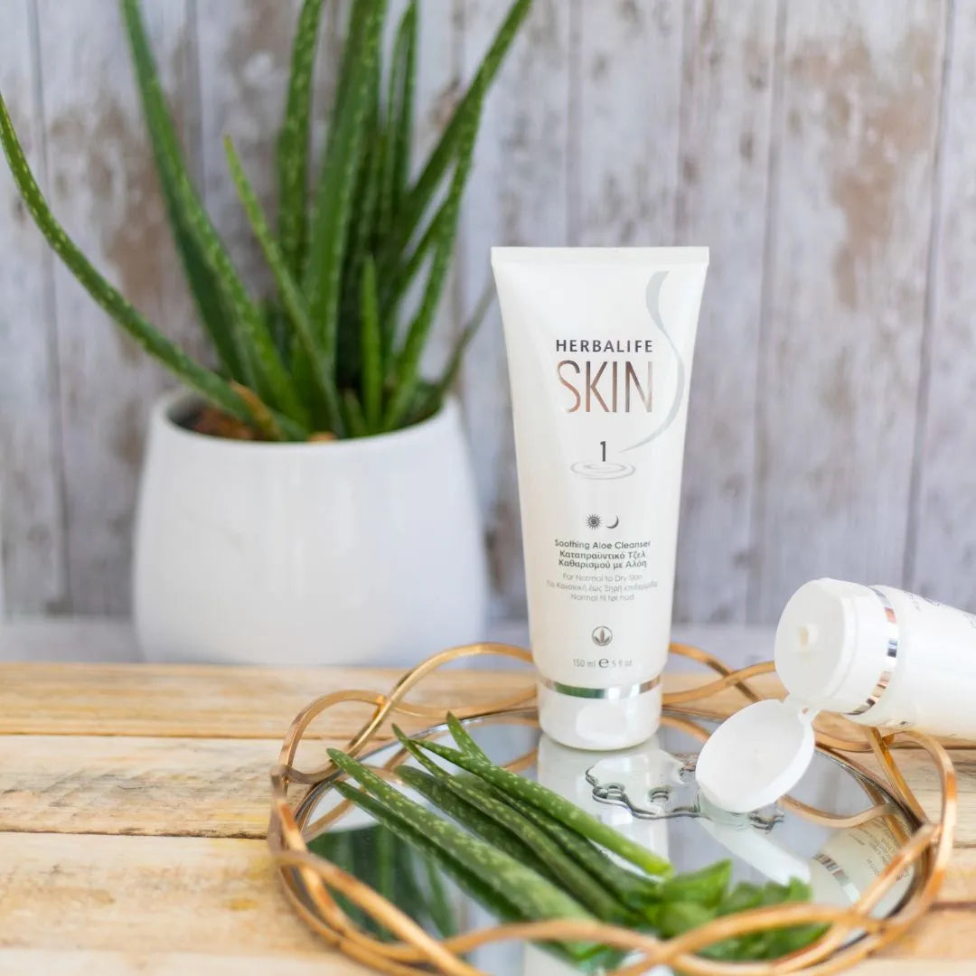 En tube Herbalife SKIN Soothing Aloe Cleanser står på et glassfat med noen avskårne aloevera-blader.