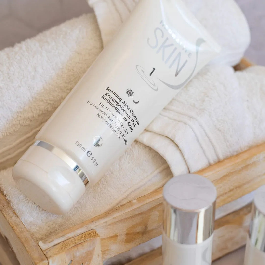 En tube Herbalife SKIN Soothing Aloe Cleanser ligger på hvite håndklær i en trekasse.