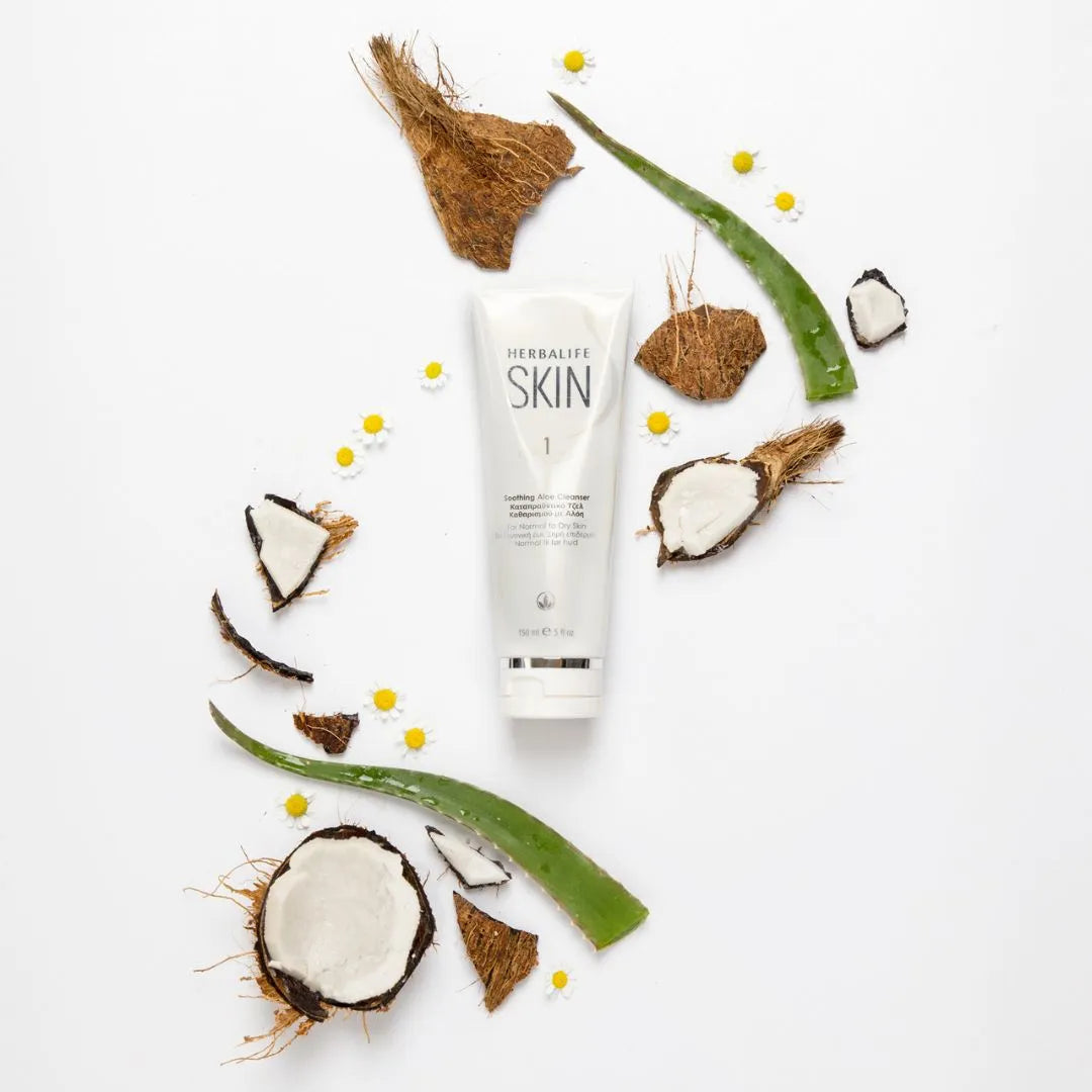 En tube Herbalife SKIN Soothing Aloe Cleanser ligger på et bord med aloeblader og kokosnøttskall.