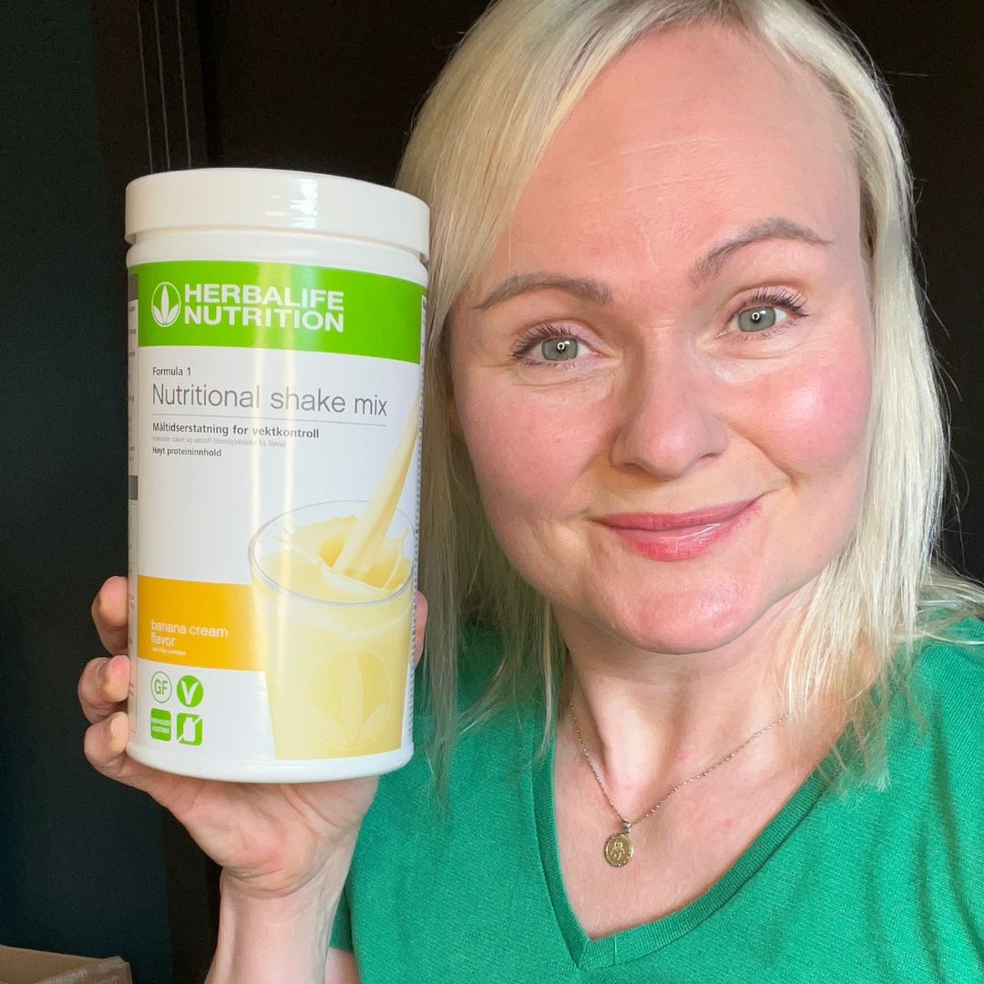 En boks Herbalife-shake banan - Formula 1 shakemix med banana cream-smak - og Helga som viser den frem.