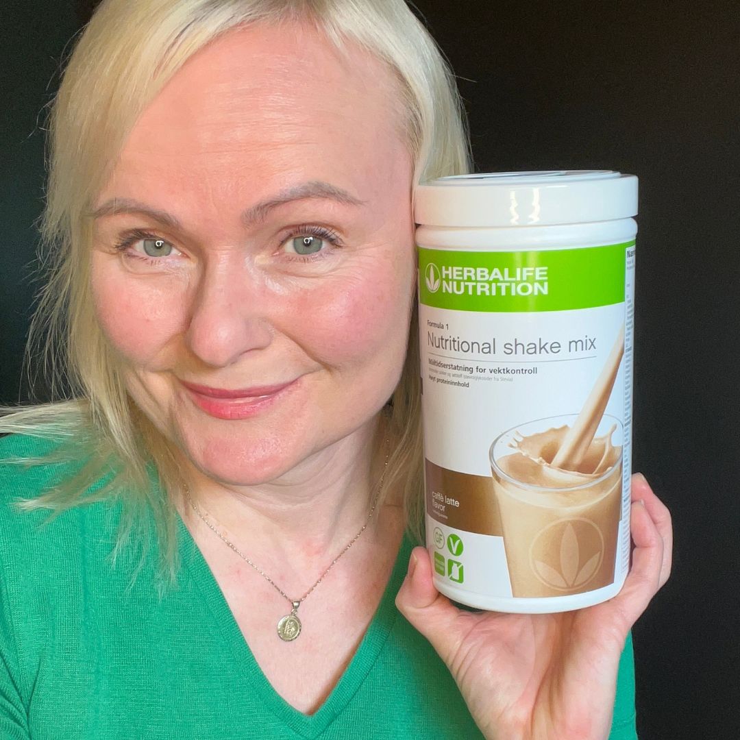 En boks Herbalife caffe latte-shake og Helga som viser den frem.