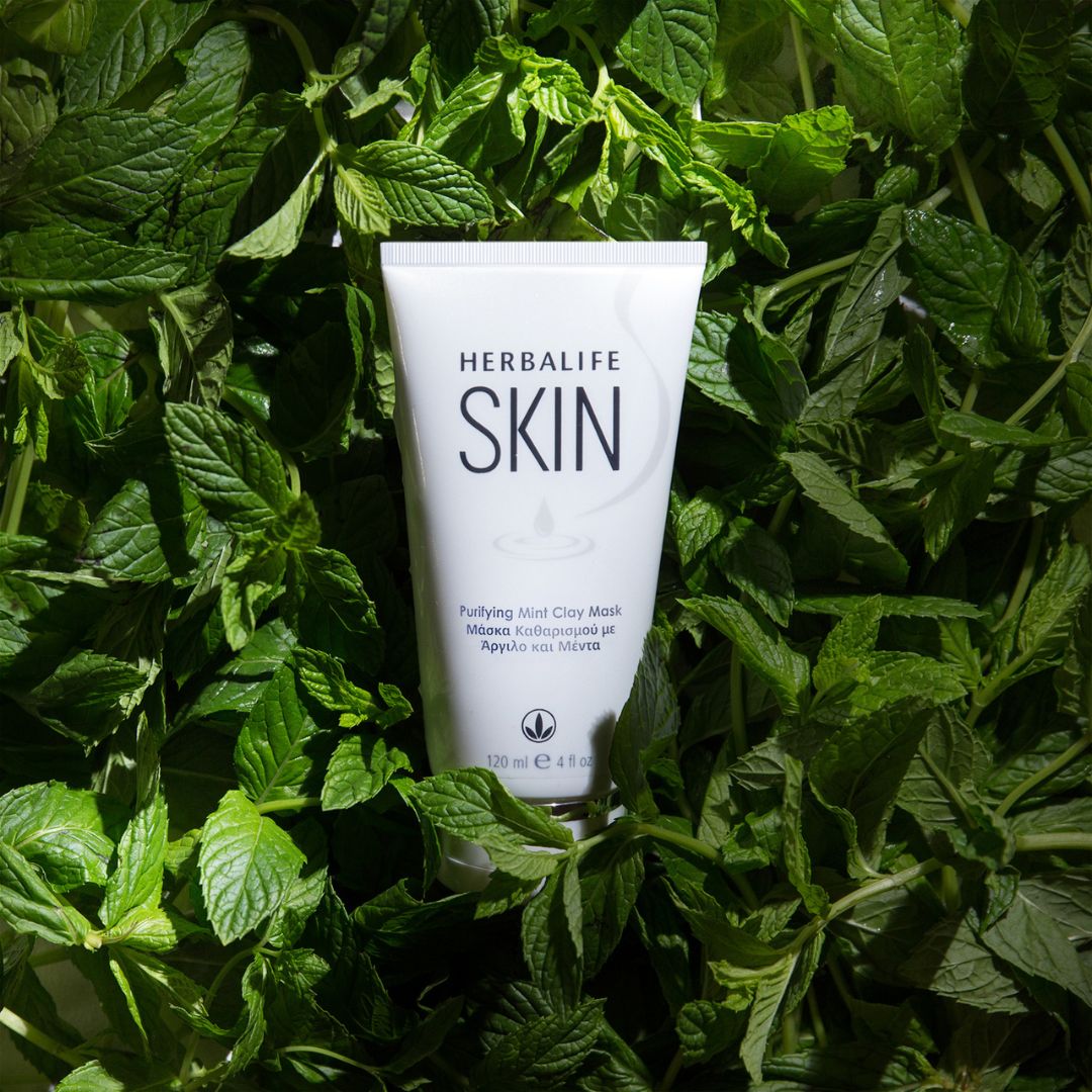 En tube Herbalife SKIN Purifying Mint Clay Mask grønn ansiktsmaske i et hav av mynte.