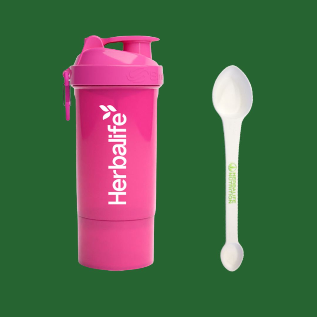 Rosa Herbalife SmartShake 600 ml med hvit logo og karabinkrok, plassert ved siden av en hvit Herbalife-måleskje. Produktfoto på grønn bakgrunn.