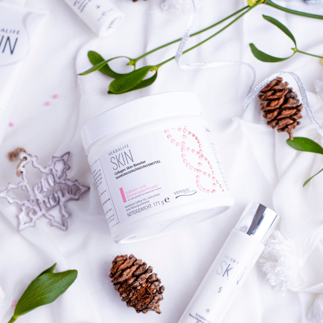 En boks Herbalife SKIN Collagen Booster  ligger sammen med SKIN hudpleieprodukter, noen kongler og stjerner på en hvit duk. 