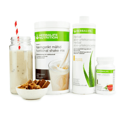 Bildet viser Herbalife-produktene som Frokostpakke basic cookie crunch består av; Herbalife-shake med cookiecrunch-smak, Herbal Aloe aloevera-juice med mangosmak og Instant urtete med original-smak samt en Herbalife-shake i et glass med sugerør og noen cookies i en skål.