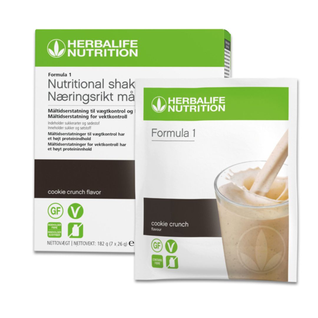 En pakke Herbalife Formula 1 shakemix porsjonsposer med cookie crunch-smak og en porsjonspose cookiecrunch. Pakken og posen er merket glutenfri, melkefri og vegansk og posen har bilde av en Herbalife-shake som helles i et glass. 