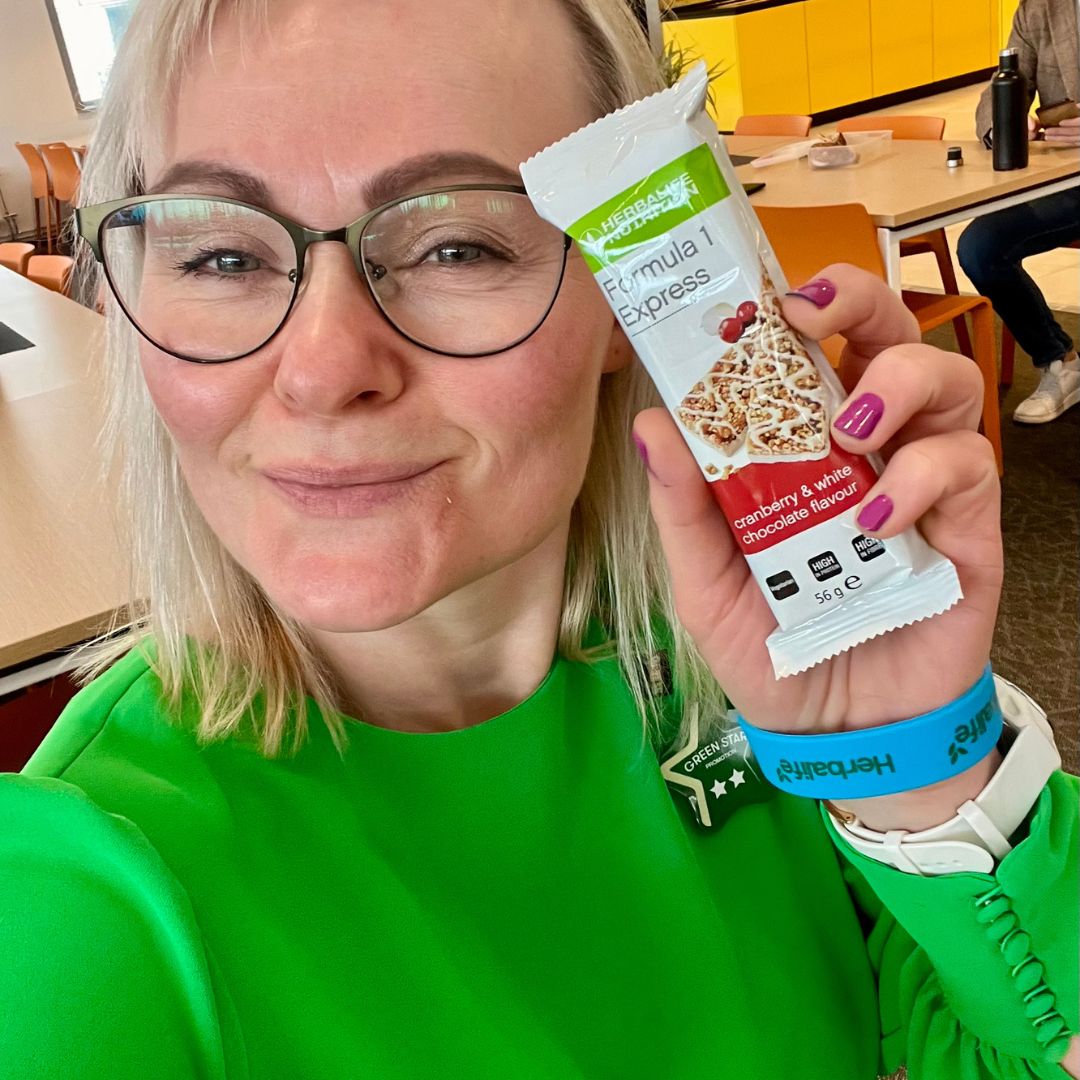 Helga i grønn kjole og en Herbalife Formula 1 Expressbar måltidsbar Tranebærsmak - Cranberry & White Chocolate flavor