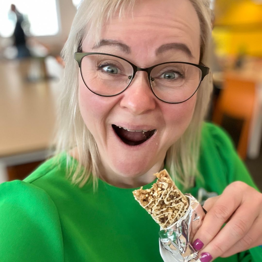 Helga i grønn kjole som spiser en Herbalife Formula 1 Expressbar måltidsbar Tranebærsmak - Cranberry & White Chocolate flavor
