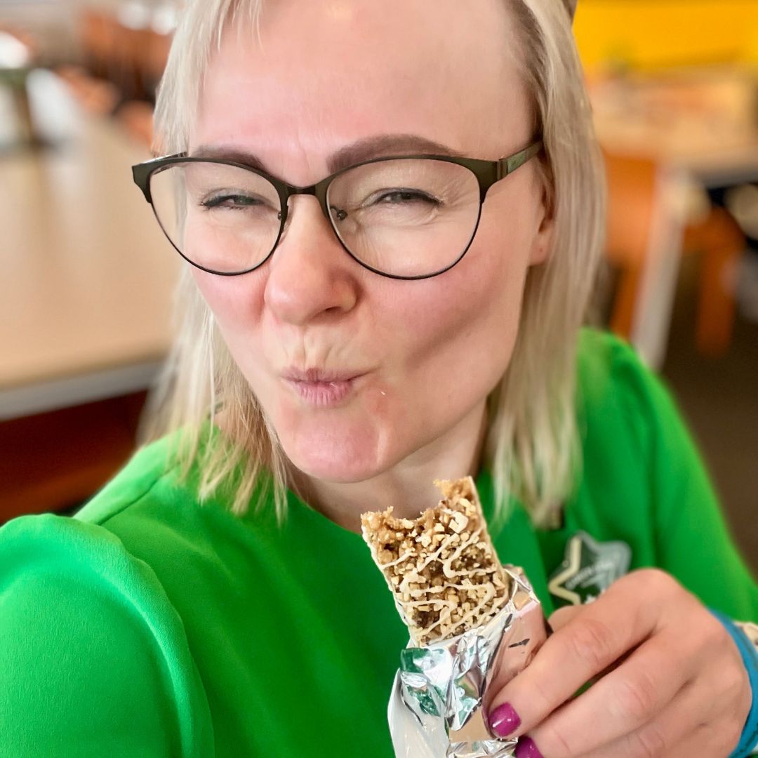 Helga i grønn kjole som spiser en Herbalife Formula 1 Expressbar måltidsbar Tranebærsmak - Cranberry & White Chocolate flavor