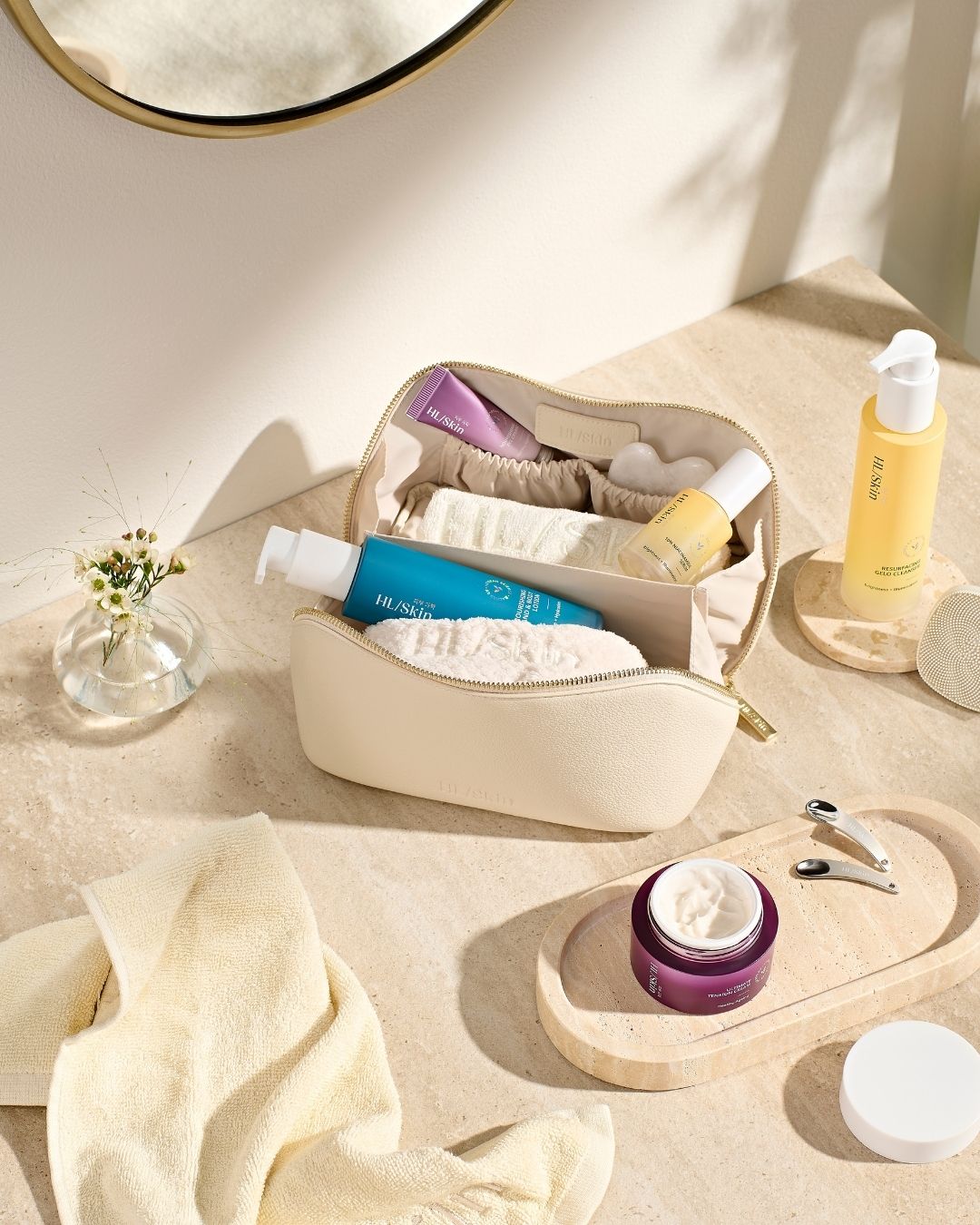 HL/Skin toalettmappe med cleanser, serum og krem, omgitt av to spatler, håndkle og hudpleietilbehør. Elegant HL/Skin-oppsett fra Herbalife på Frokostshake.no.