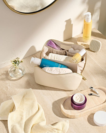 HL/Skin toalettmappe åpen på baderomsbenk, fylt med cleanser, serum, krem og hudpleietilbehør. Viser komplett HL/Skin-rutine fra Herbalife på Frokostshake.no.