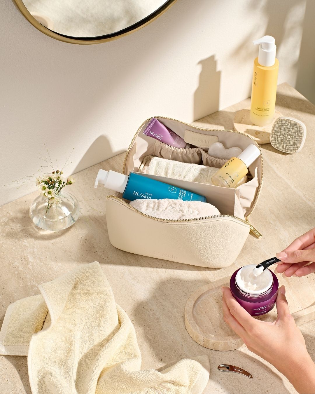 HL/Skin toalettmappe fylt med hudpleieprodukter - cleanser, serum, krem og tilbehør som håndklær og spatel. Elegant oppsett på baderomsbenk fra Herbalife på Frokostshake.no.
