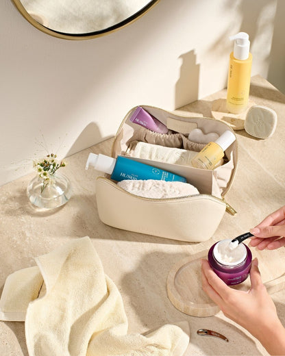 HL/Skin toalettmappe fylt med hudpleieprodukter - cleanser, serum, krem og tilbehør som håndklær og spatel. Elegant oppsett på baderomsbenk fra Herbalife på Frokostshake.no.