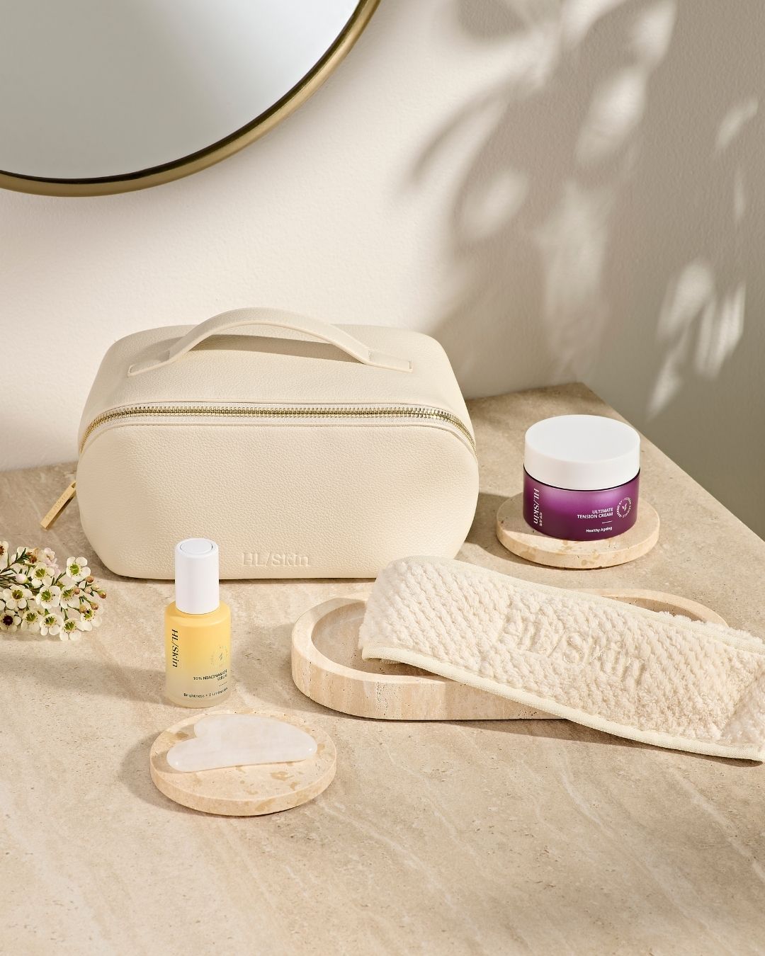 HL/Skin toalettmappe i vegansk skinn sammen med hårbånd, Gua Sha-stein, serum og ansiktskrem. Elegant oppsett på baderomsbenk som viser hudpleietilbehør fra Herbalife på Frokostshake.no.