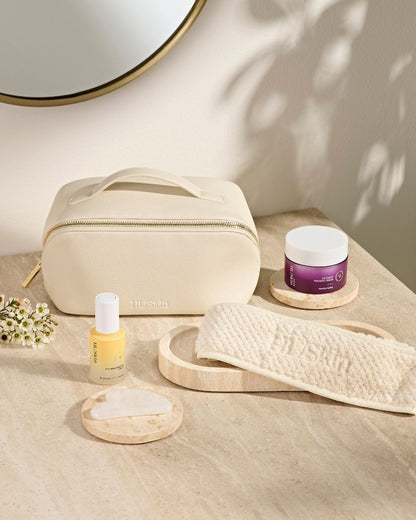 HL/Skin toalettmappe i vegansk skinn sammen med hårbånd, Gua Sha-stein, serum og ansiktskrem. Elegant oppsett på baderomsbenk som viser hudpleietilbehør fra Herbalife på Frokostshake.no.