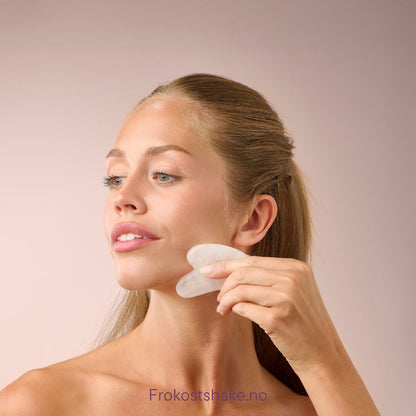 Kvinne masserer kjevepartiet med Herbalife HL/Skin Gua Sha laget av hvit jade. Beroligende ansiktsmassasje som fremmer glød og velvære fra Frokostshake.no.