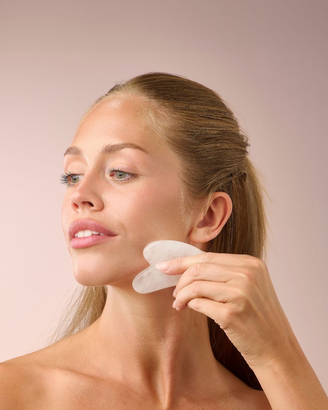 Kvinne masserer kjevepartiet med Herbalife HL/Skin Gua Sha laget av hvit jade. Beroligende ansiktsmassasje som fremmer glød og velvære fra Frokostshake.no.