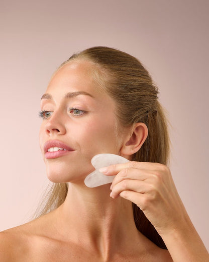 Kvinne masserer kjevepartiet med Herbalife HL/Skin Gua Sha laget av hvit jade. Beroligende ansiktsmassasje som fremmer glød og velvære fra Frokostshake.no.