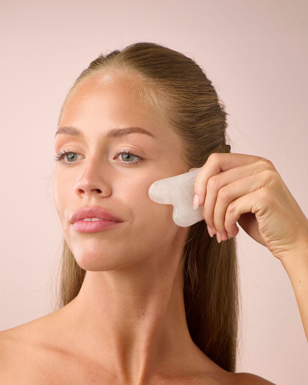 Kvinne bruker Herbalife HL/Skin Gua Sha i hvit jade til ansiktsmassasje. Beroligende og glødgivende hudpleierituale fra Frokostshake.no.