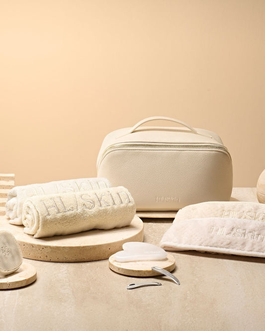 HL/Skin toalettmappe i vegansk skinn sammen med håndklær, hårbånd, Gua Sha, spatler og ansiktsbørste. Komplett hudpleietilbehør fra Herbalife på Frokostshake.no vist på benk.