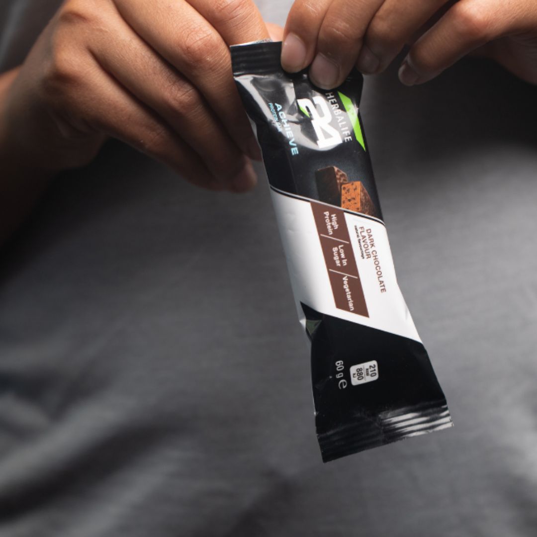 Nærbilde av person som holder en Herbalife H24 Achieve Proteinbar i smaken mørk sjkokolade - proteinrik snack med lavt sukkerinnhold, perfekt før eller etter trening. 