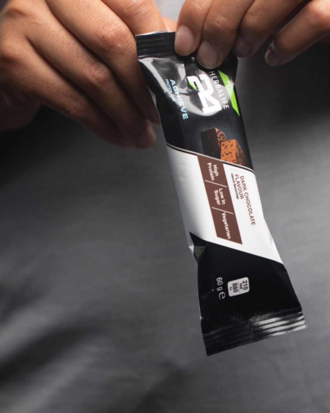 Nærbilde av person som holder en Herbalife H24 Achieve Proteinbar i smaken mørk sjkokolade - proteinrik snack med lavt sukkerinnhold, perfekt før eller etter trening. 