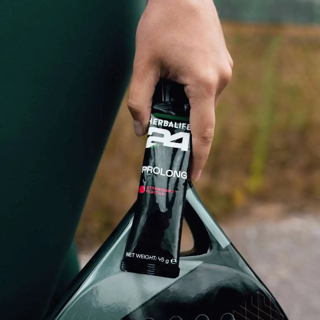 En person i treningstøy med en porsjonspose Herbalife H24 Prolong Energy Gel og en racket i hånda.