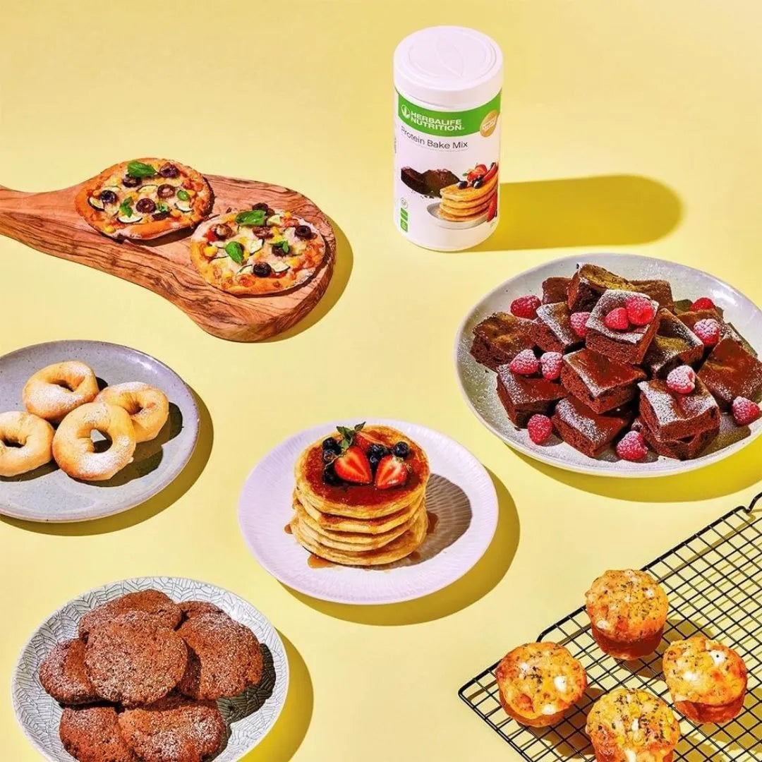 En boks Herbalife Protein Bake Mix sammen med eksempler på ulike retter laget med bakemiksen; pizza, smultringer, sjokoladecookies, amerikanske pannekaker, brownies og muffins.