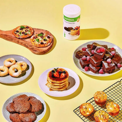 En boks Herbalife Protein Bake Mix sammen med eksempler på ulike retter laget med bakemiksen; pizza, smultringer, sjokoladecookies, amerikanske pannekaker, brownies og muffins.