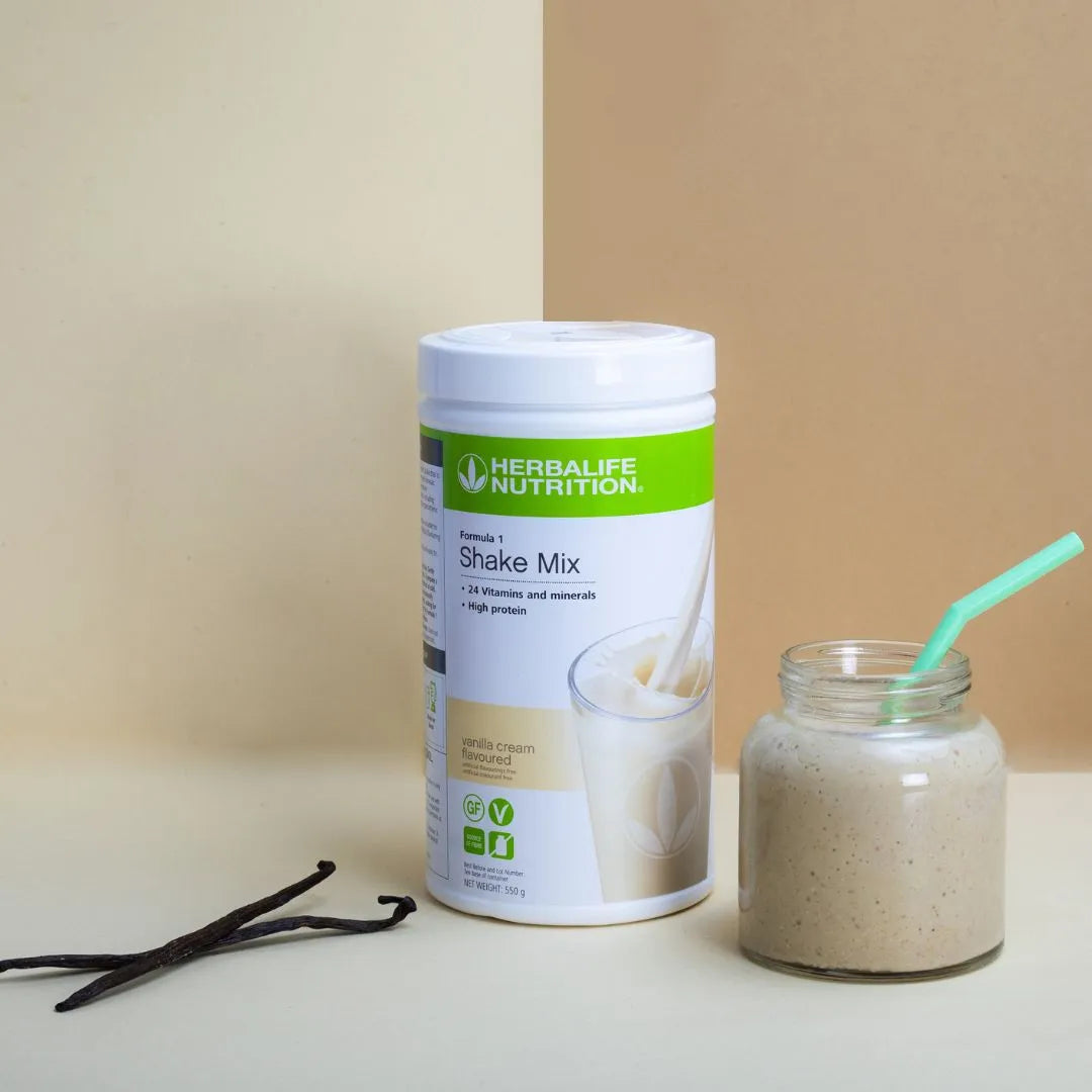 Boks Herbalife Formula 1 shakemix med vaniljesmak i midten, glasskrus med smoothie og mintgrønt sugerør og to vaniljestenger.