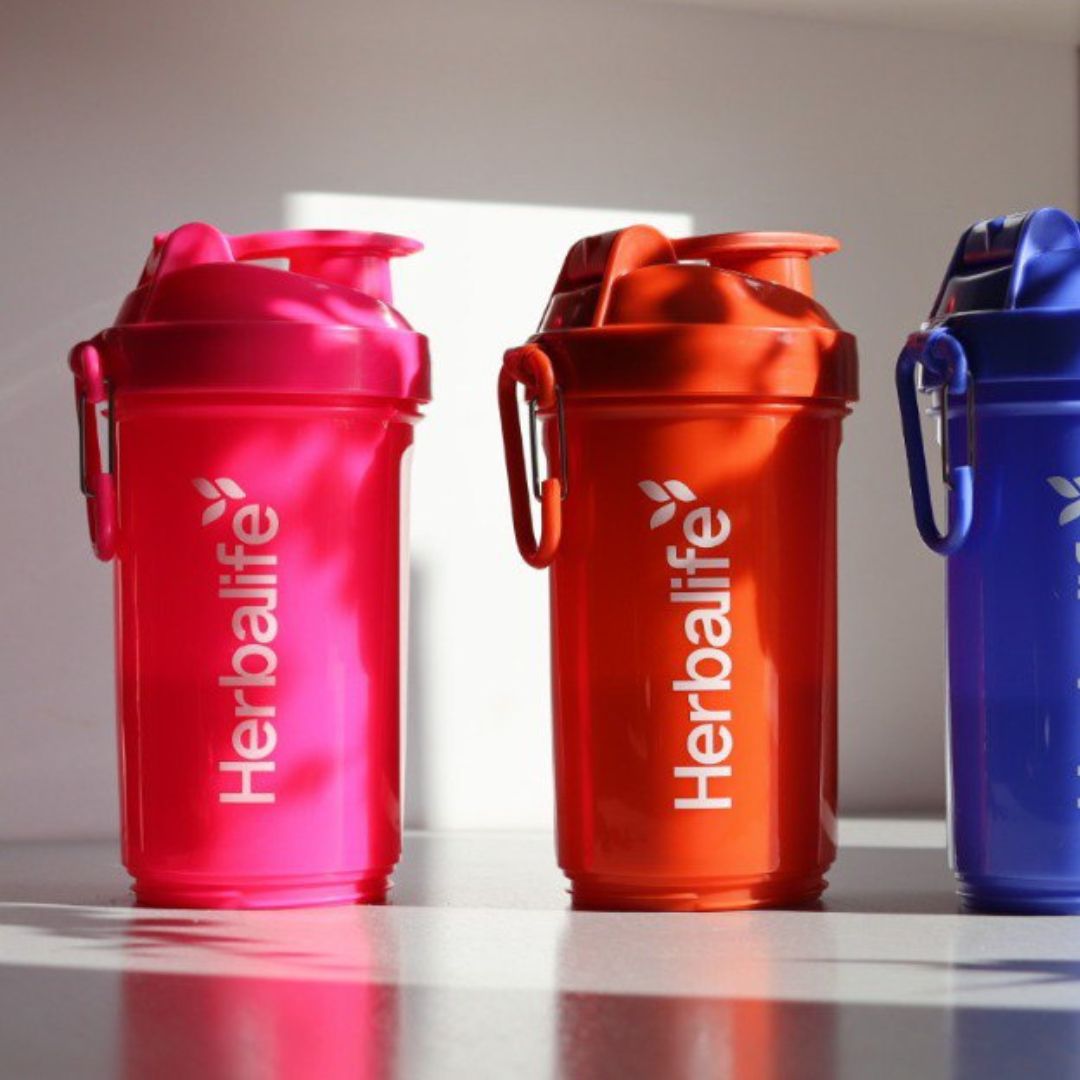 Tre Herbalife Smartshake-flasker på rekke i rosa, oransje og blå farge, hver med hvit Herbalife-logo og karabinkrok.