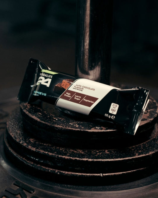 Herbalife H24 Achieve Protein Bar i smaken mørk sjokolade, plassert på vektskiver - perfekt snack etter trening med høyt proteininnhold og lavt sukkerinnhold.