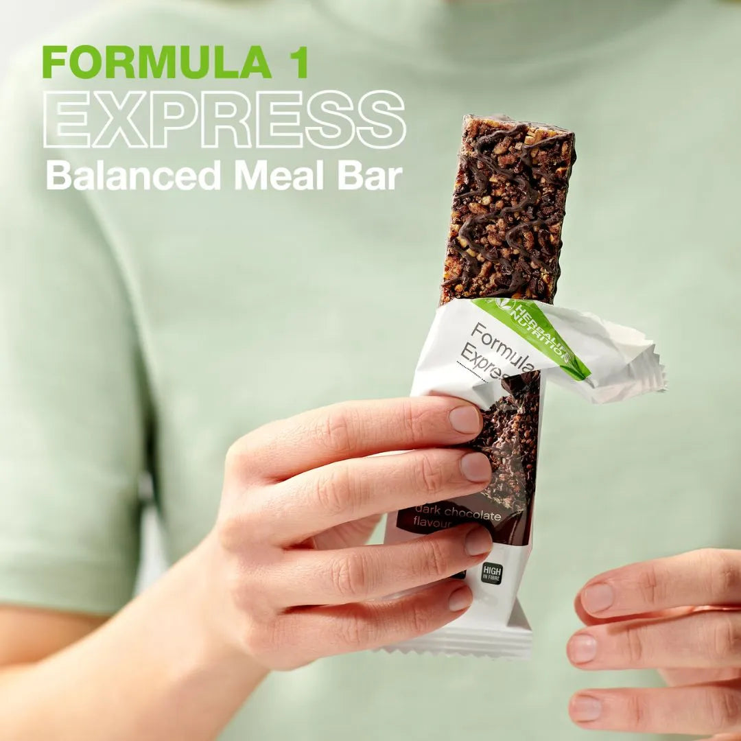 En person i lys grønn t-skjorte holder en åpnet Herbalife Formula 1 mellombar med mørk sjokolade. På bildet står teksten "Formula 1 Express Balanced Meal Bar".