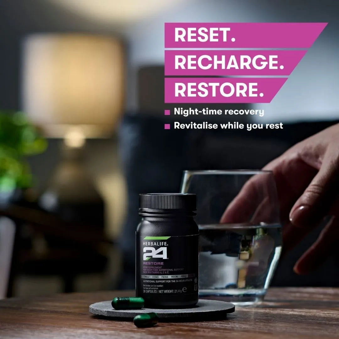 En hånd strekker seg mot et glass vann som står sammen med en boks Herbalife H24 Restore kosttilskudd. Det ligger to løse kapsler foran boksen. På bildet står teksten “Reset. Recharge. Restore. Night-time recovery. Revitalise while you rest.”