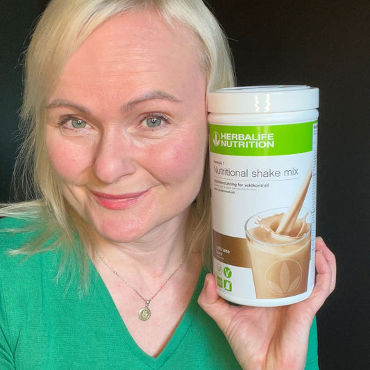En boks Herbalife caffe latte-shake og Helga som viser den frem.