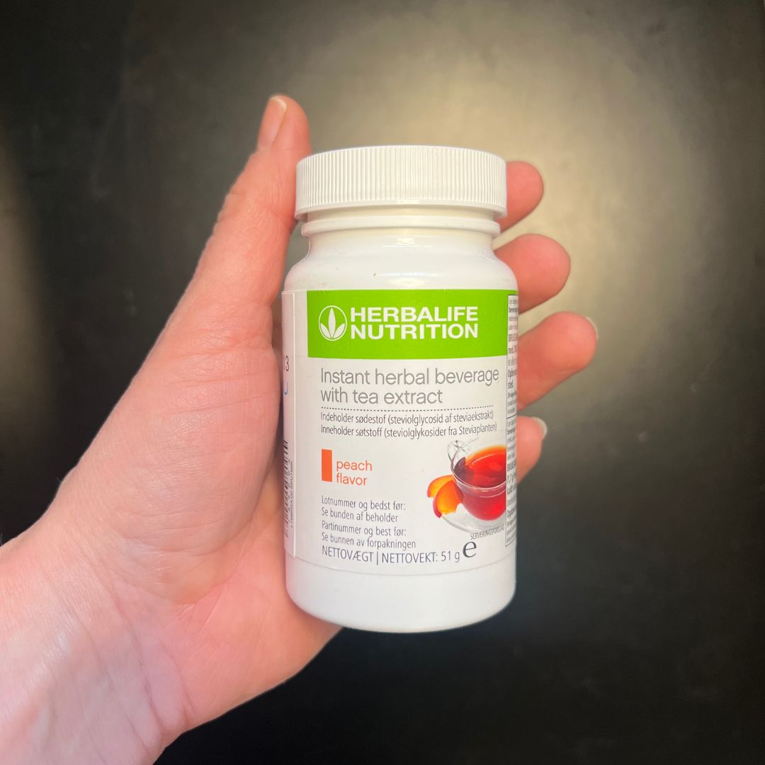 En boks Herbalife Instant Peach urtekonsentrat te med ferskensmak, 51 gram, i hånda.