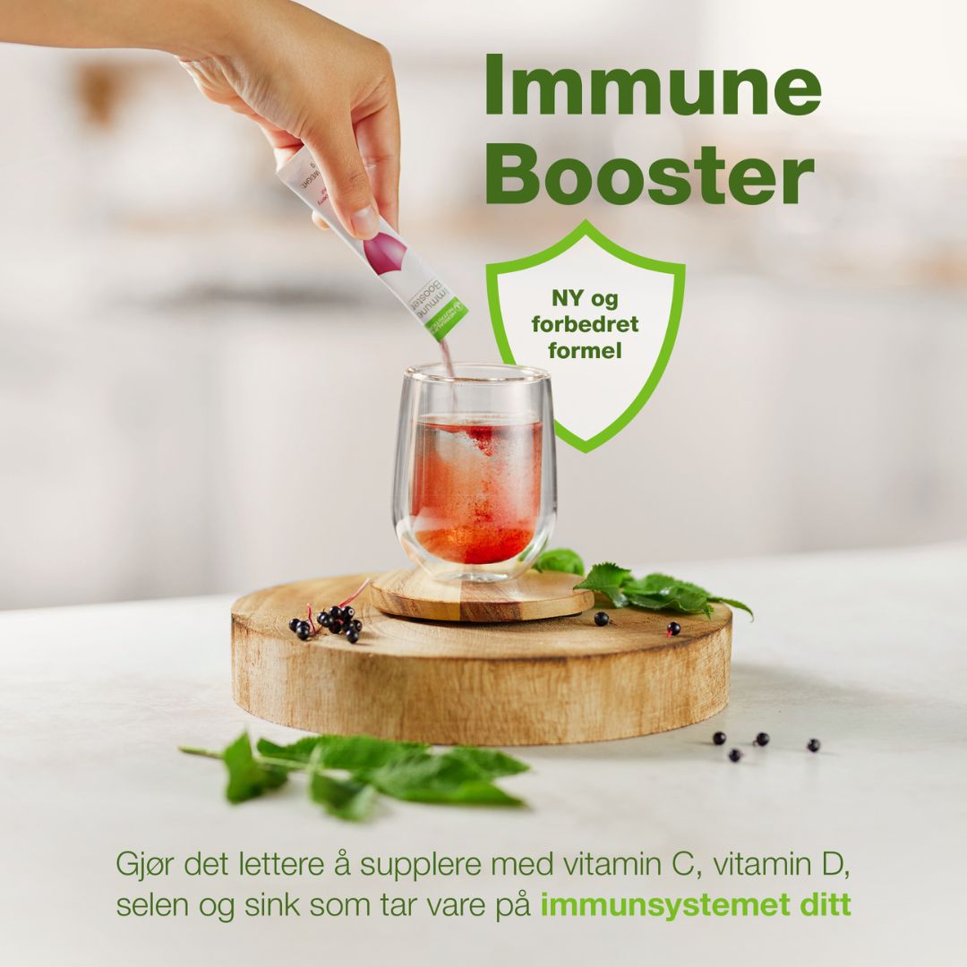 En person heller en porsjonspose Immune Booster i et glass vann og på bildet står det "Immune Booster. NY og forbedret formel. Gjør det lettere å supplere med vitamin c, vitamin d, selen og sink som tar vare på immunsystemet ditt".