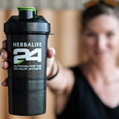 En kvinne holder opp og frem en svart supershaker med Herbalife H24-logo. 