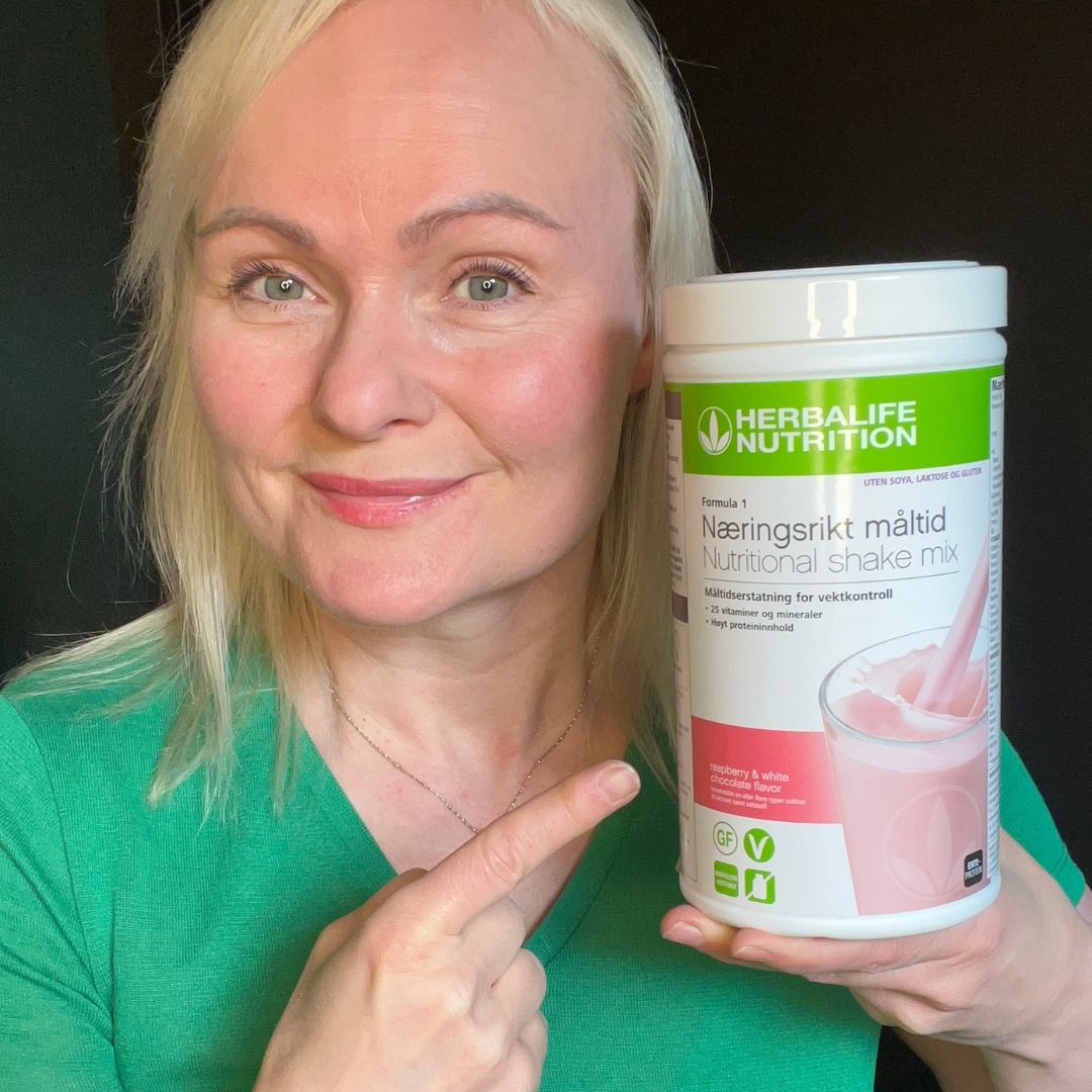 En boks Herbalife Formula 1 soyafri shakemix med Raspberry & White Chocolate-smak og Helga som peker på boksen.