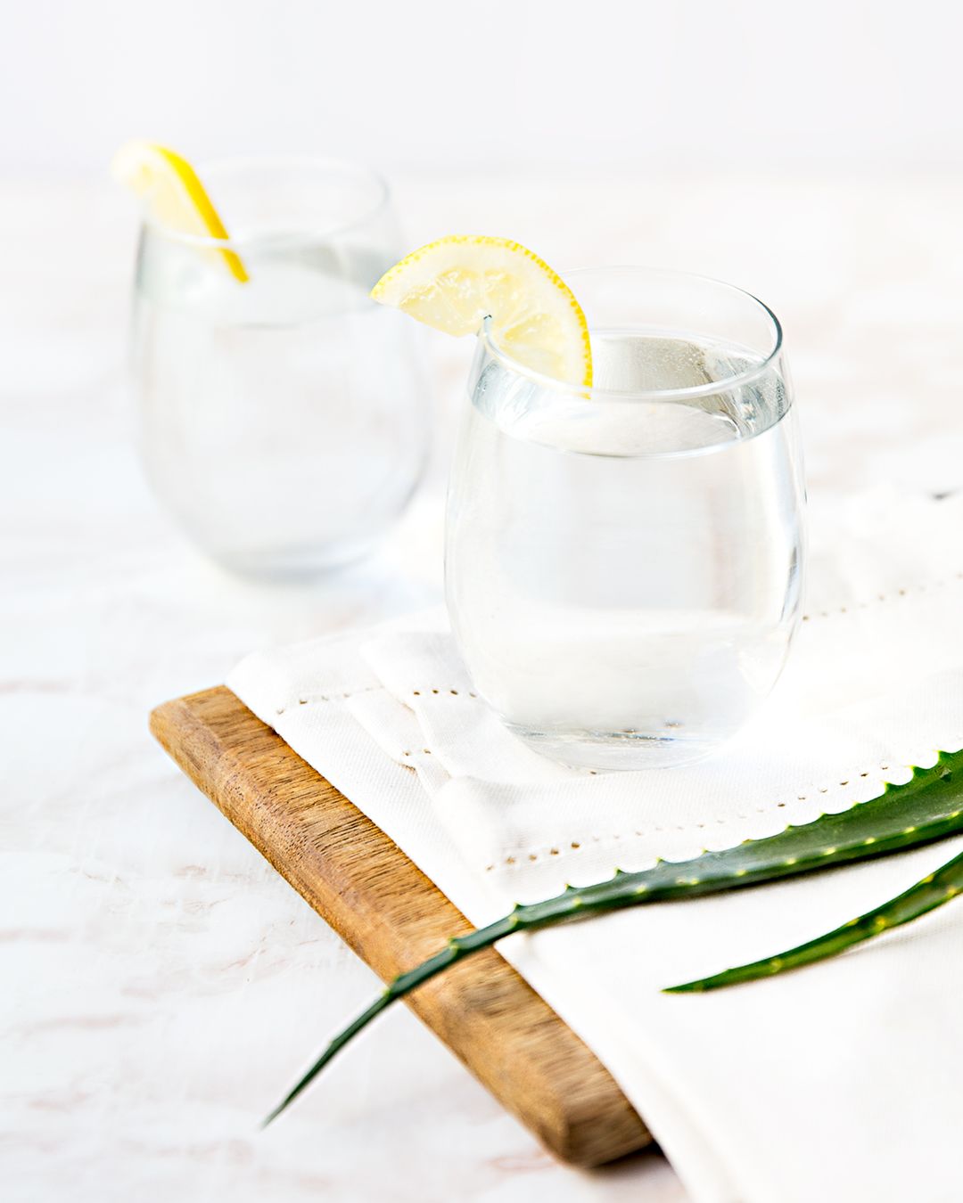 To glass Herbalife Herbal Aloe aloevera-juice pyntet med skivet sitron på ei trefjøl med aloe vera-blader.