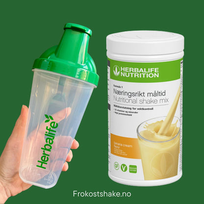 Banan Herbalife shake-boks og shakerflaske i hånden på grønn bakgrunn, Frokostshake.no. 