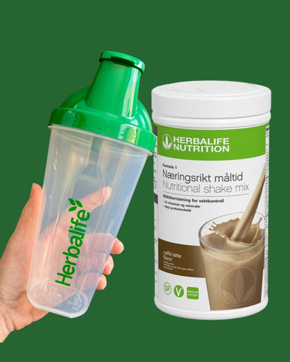Caffe latte Herbalife shake-boks og shakerflaske i hånden på grønn bakgrunn, Frokostshake.no. 