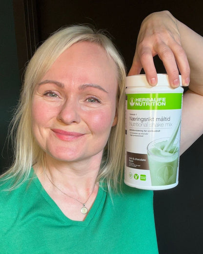 Helga holder Herbalife Formula 1 mintssjokolade boks og smiler mot kamera