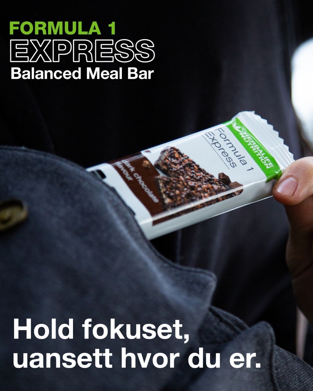 En person i en mørkeblå jakke tar en Herbalife Formula 1 mellombar med mørk sjokolade opp av jakkelomma. På bildet står teksten "Formula 1 Express Balanced Meal Bar".