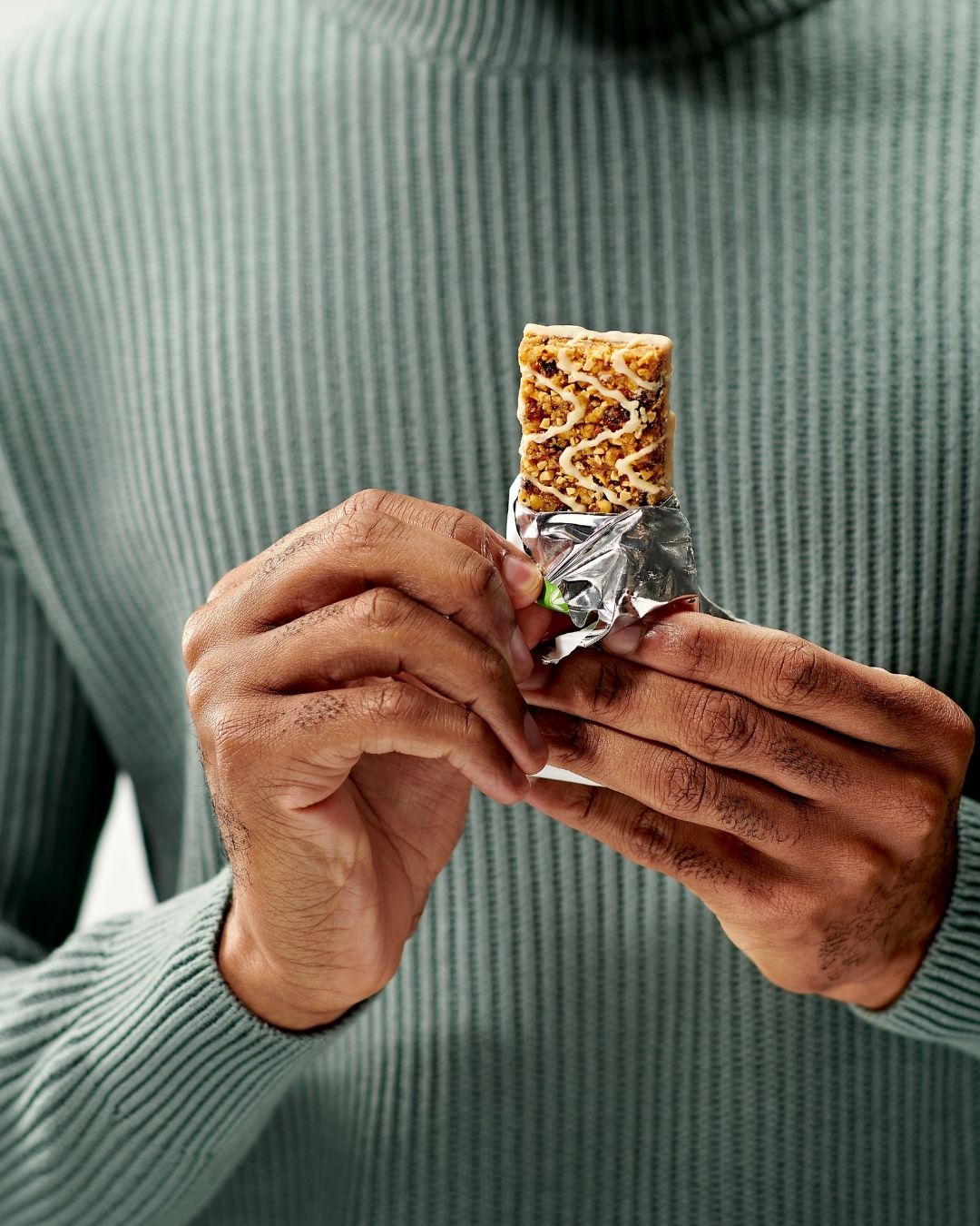 En person holder en måltidsbar i hendene og skal til å ta en bit av den.