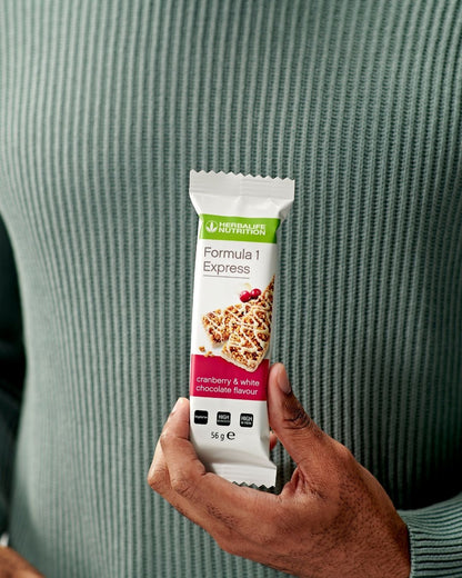 En person holder en innpakket Herbalife Formula 1 Express måltidsbar tranebær og hvit sjokolade i hendene og viser den frem til oss.