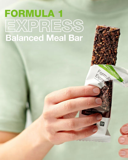 En person i lys grønn t-skjorte holder en åpnet Herbalife Formula 1 mellombar med mørk sjokolade. På bildet står teksten "Formula 1 Express Balanced Meal Bar".